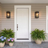 A modern farmhouse entry with two Barlow Outdoor Wall Lights in textured black flanking a white front door on tan siding with ferns and hydrangeas at twilight.