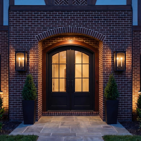 An outdoor entryway featuring two Barlow textured black lanterns flanking dark arched double doors on a red brick facade with square stone pavers.