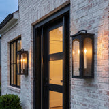 A modern farmhouse entryway featuring two Barlow Outdoor Wall Light lanterns in textured black flanking a black front door on a whitewashed brick exterior.