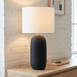 A modern living room featuring the Nolette Large Table Lamp 29", Textured Black with a white linen shade on a light wood console against a white brick wall.