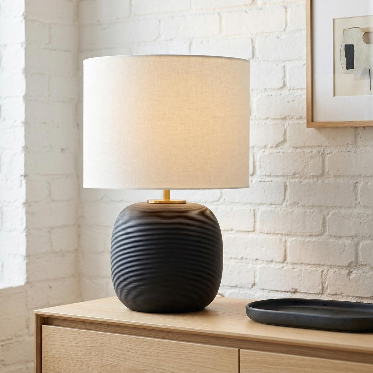 Nolette Medium Table Lamp 23", Textured Black globe Table Lamp in a Modern Living Room with an oak console and white brick wall.