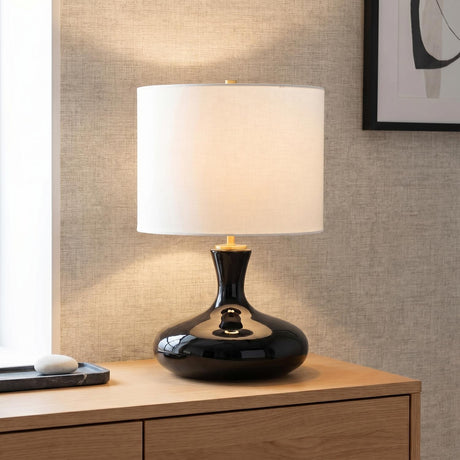 A contemporary living room with the Moselle Table Lamp 21", Glossy Black with brushed brass accents and a linen shade on a wood dresser against textured wallpaper.