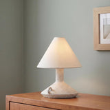A minimalist bedroom featuring the Gemina Rechargeable Table Lamp 12", Artisan Ceramic White with a linen shade placed on a warm wood dresser against sage green walls.