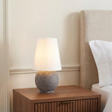 A contemporary bedroom featuring the Inara Rechargeable Table Lamp 15", Artisan Ceramic Gray with a white linen shade on a fluted walnut nightstand beside a beige headboard.