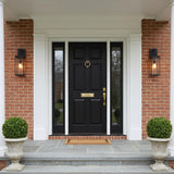 A colonial red brick entry with two Lavelle Outdoor Wall Light, Medium 22", Textured Black lanterns glowing while flanking a black front door with boxwood topiaries.