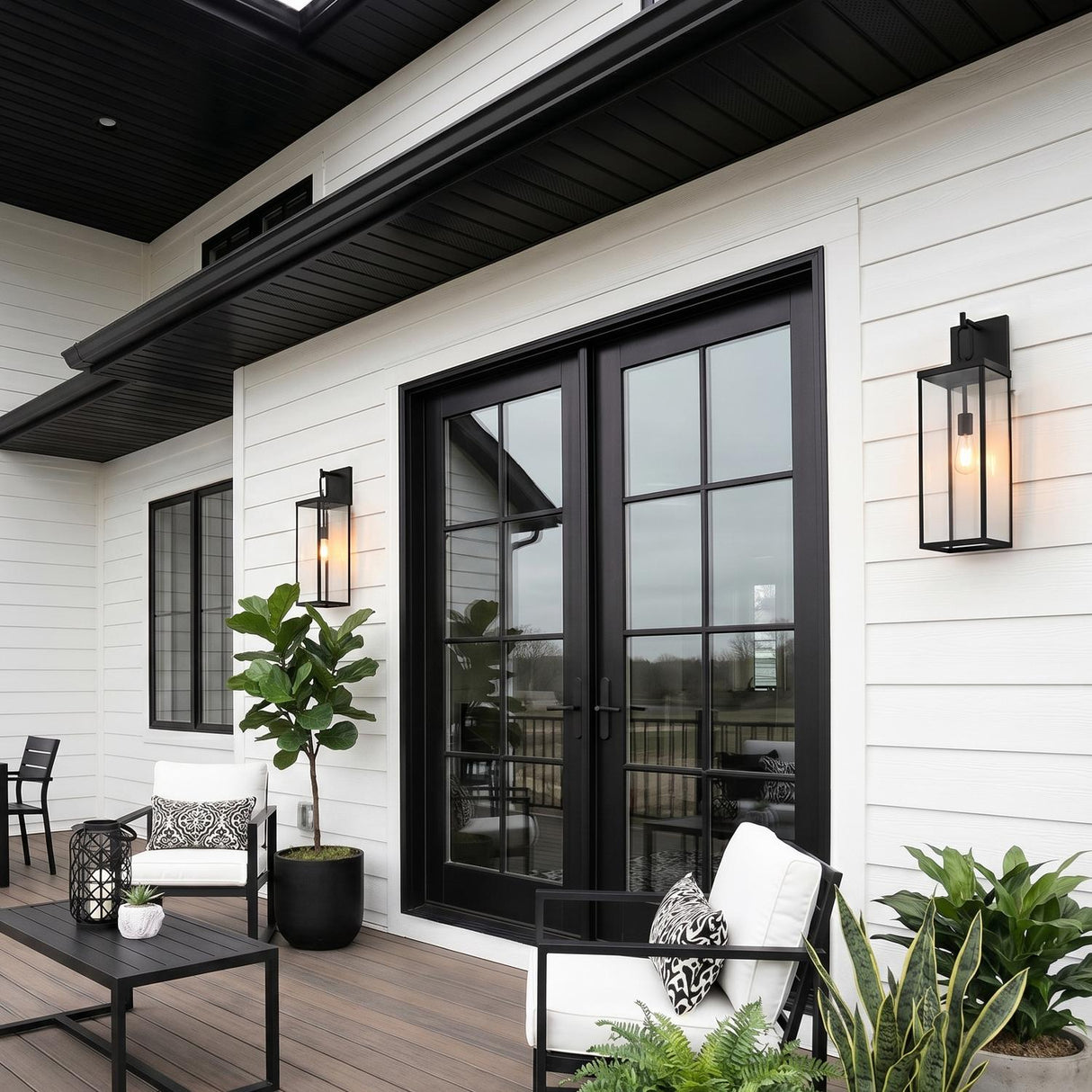 A modern farmhouse patio with the Lavelle Outdoor Wall Light, Large 25", Textured Black flanking black French doors on white siding at dusk with outdoor furniture.