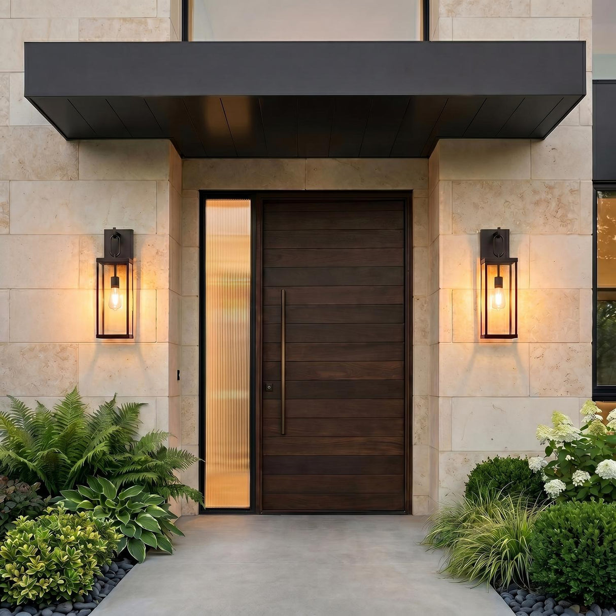 A modern home entry featuring two glowing Lavelle Outdoor Wall Lights in old bronze flanking a dark wood front door on a limestone wall with ferns.
