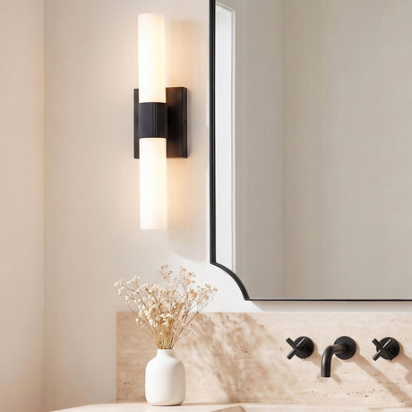 A modern bathroom with a Ramsey LED Vanity Light 18" in matte black and frosted glass mounted beside a mirror over a travertine countertop with cross-handle faucets.