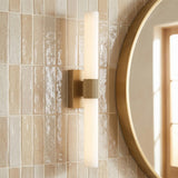 A modern bathroom with a Ramsey LED Vanity Light 24" in satin brass and frosted glass mounted on beige vertical tiles beside a round gold mirror.