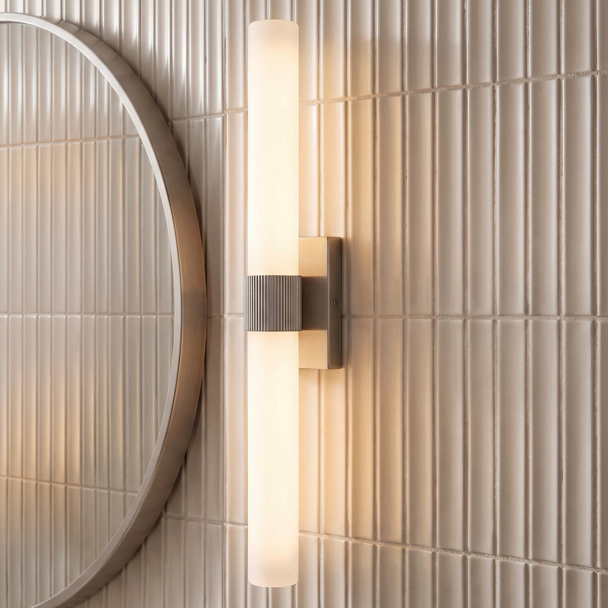A modern bathroom with a Ramsey LED Vanity Light 30", Brushed Nickel featuring frosted glass, mounted on vertical fluted tiles beside a round brushed nickel mirror.