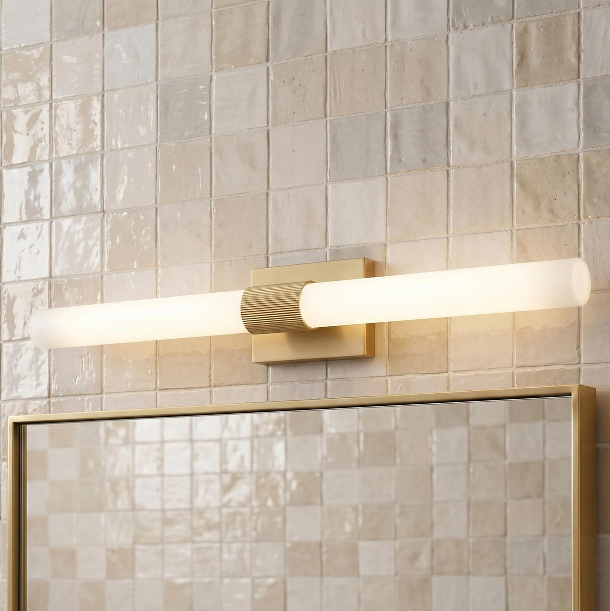 A contemporary bathroom with the Ramsey LED Vanity Light 36-inch Satin Brass featuring a frosted glass tube over a brass-framed mirror and beige zellige tile.