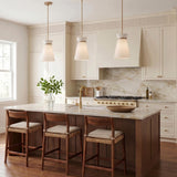 A transitional kitchen features three Veronica Pendant 10-inch fixtures in satin brass and white linen over a marble-topped walnut island with woven wood bar stools.