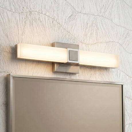 A modern bathroom features a Wendell LED Vanity Light 18", Brushed Nickel with frosted glass mounted over a framed mirror against wavy textured white wallpaper.
