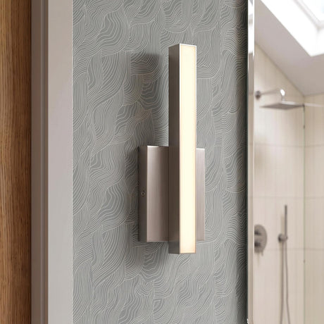 A modern bathroom with a Garrison LED Wall Sconce 13", Brushed Nickel mounted on gray textured wallpaper beside a mirror reflecting a sloped ceiling and shower.