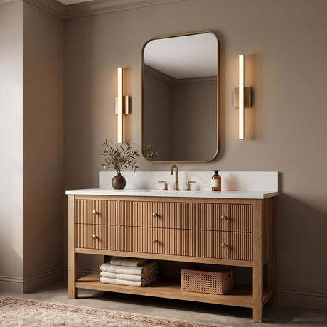 A contemporary bathroom with two satin brass Garrison LED Vanity Lights flanking a rounded mirror above a fluted wood vanity with a white marble countertop.
