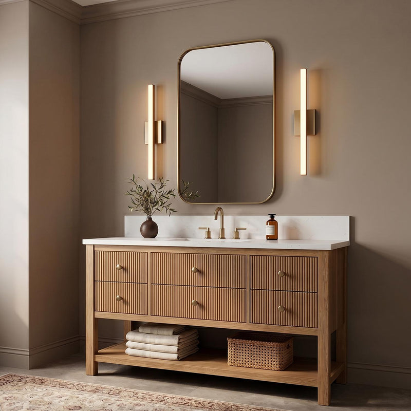 A contemporary bathroom with two satin brass Garrison LED Vanity Lights flanking a rounded mirror above a fluted wood vanity with a white marble countertop.