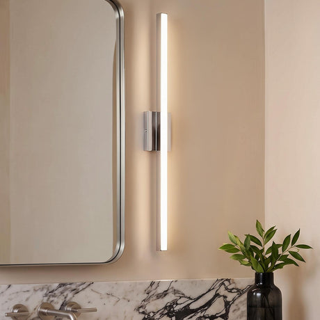 A modern bathroom with a chrome linear vanity bar mounted beside a rounded silver mirror above a white marble backsplash and a small potted plant.