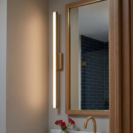 A modern bathroom with a satin brass Garrison LED Vanity Light 36" mounted beside a wood-framed mirror above a marble counter and brass faucet.