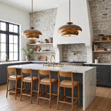 A modern farmhouse kitchen featuring two Garnett Large Pendants in vintage gilded brass over a marble waterfall island with charcoal cabinets and a stone wall.
