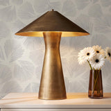 A modern living room with the Darnell Table Lamp 21", Vintage Brass on a white console table against gray fan patterned wallpaper and white flowers.