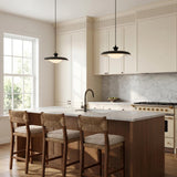 A transitional kitchen featuring two matte black and opal glass saucer pendants over a wood island with white marble counters and woven bar stools.