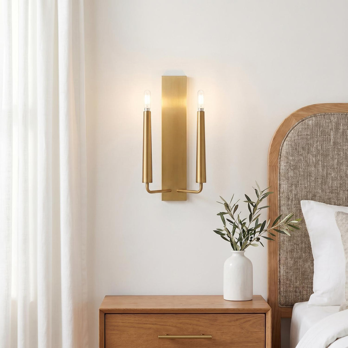 A modern bedroom featuring the Solana Double Wall Sconce 18", Modern Brass on a white wall above a wooden nightstand and a linen-upholstered oak headboard.