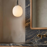 A contemporary bathroom featuring the Basile Small Pendant in matte black with ribbed milk glass hanging over a dark veined marble vanity with brass fixtures.