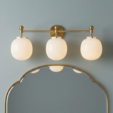 A mid-century bathroom with the Basile 3 Light Vanity in brushed brass and ribbed milk glass installed above a gold scalloped mirror on a blue wall.