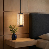 A modern bedroom with an urban bronze and clear ribbed glass pendant hanging over a floating wood nightstand beside a black textured headboard and oak wall panels.