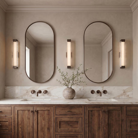 A transitional bathroom with three urban bronze and clear ribbed glass wall sconces flanking two oval mirrors above a white marble double vanity and wood cabinets.