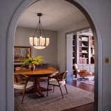 A mid-century dining room with the Dagan LED Chandelier 30", Urban Bronze over a round walnut table and cane-back chairs visible through an arched doorway.