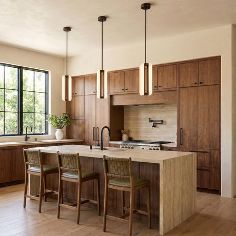 A modern kitchen with three Dagan LED Pendants in urban bronze and frosted glass over a travertine waterfall island featuring walnut cabinetry and leather barstools.