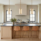 A modern farmhouse kitchen with three vintage brass Dagan LED Pendants over a light wood island with woven rattan stools and a marble backsplash.