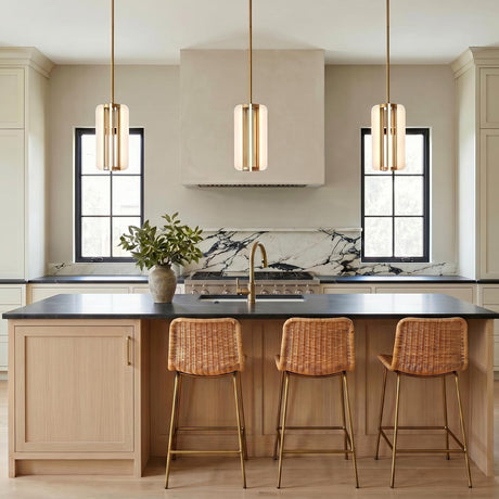 A modern farmhouse kitchen with three vintage brass Dagan LED Pendants over a light wood island with woven rattan stools and a marble backsplash.