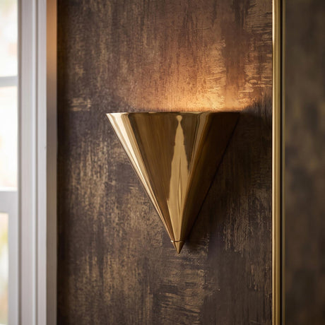 A contemporary foyer with the Zora Wall Sconce 8", Polished Brass mounted on a textured metallic wall beside a white window frame and gold-framed mirror.