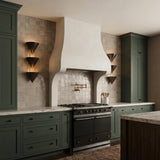 A contemporary kitchen with dark green cabinetry and two Zora 3 Light Wall Sconces in urban bronze flanking a white plaster range hood over glossy square tile.