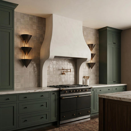 A contemporary kitchen with dark green cabinetry and two Zora 3 Light Wall Sconces in urban bronze flanking a white plaster range hood over glossy square tile.