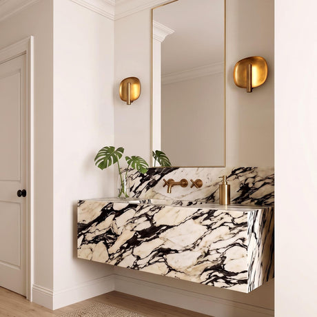 A contemporary bathroom with two Orlene LED Wall Sconce 8", Vintage Brass fixtures flanking a mirror above a floating black and white veined marble vanity.