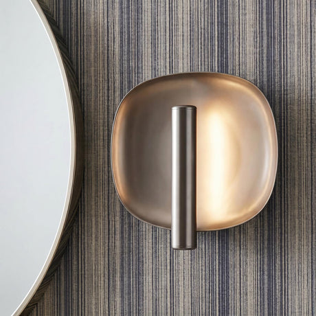 A modern bathroom with a pewter Orlene LED Wall Sconce featuring a metallic saucer backplate flanking a round mirror on textured gray pinstripe wallpaper.
