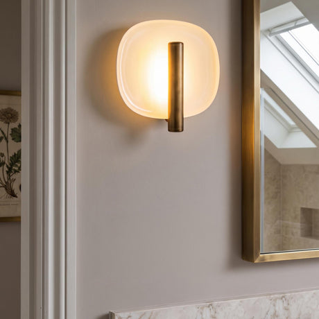 A contemporary bathroom with the Orlene LED Wall Sconce 8 inch in vintage brass and pearl white glass mounted beside a brass mirror and marble counter.