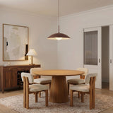 A mid-century dining room features the Lenora Metal Pendant 19", Maroon over a round walnut pedestal table, surrounded by boucle chairs and a dark wood sideboard.