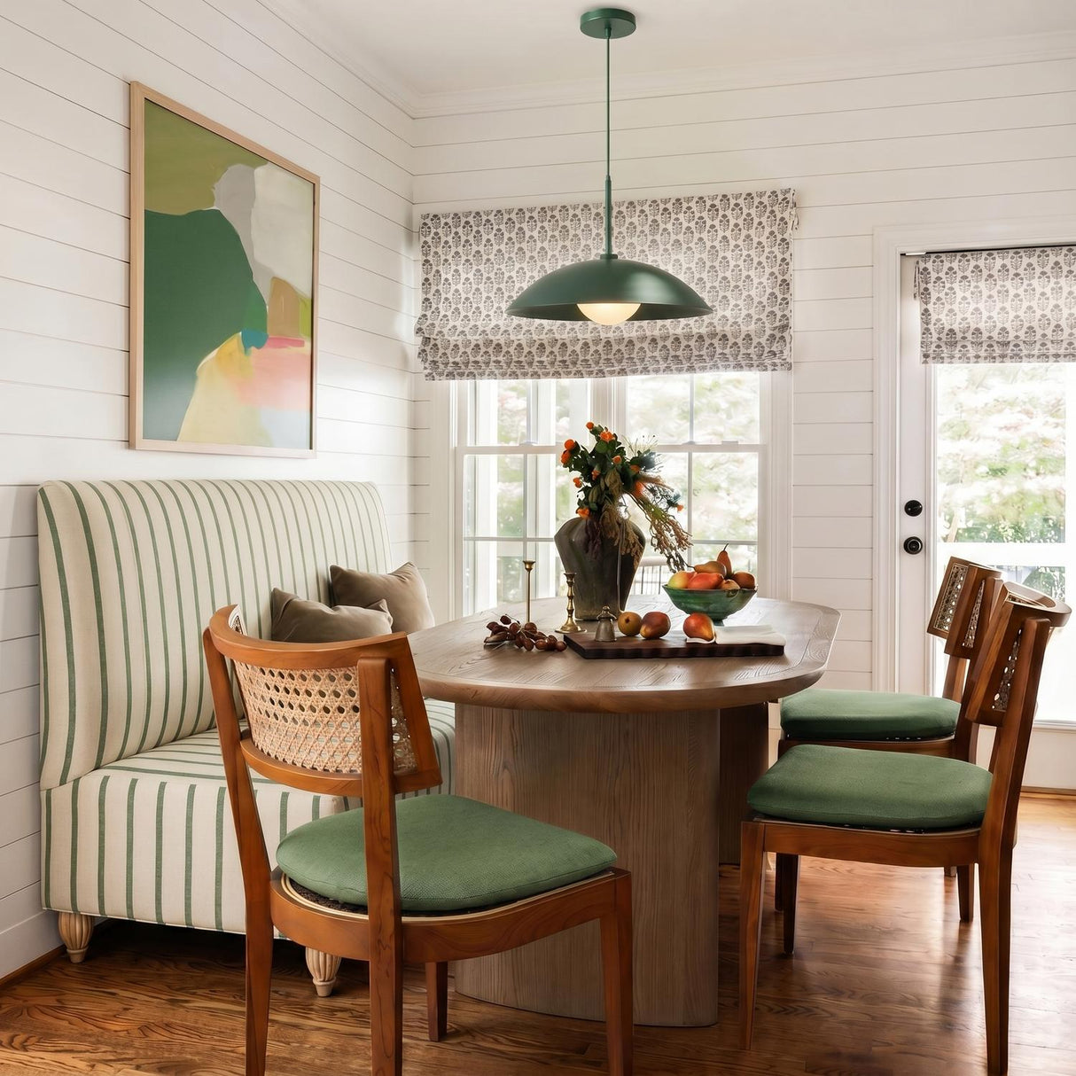A farmhouse dining room with a Lenora Metal Pendant 19", Hunter Green over a wooden oval table featuring a striped banquette and white shiplap walls.