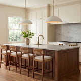 A transitional kitchen with two matte white and brushed brass Charlie Pendants over a white marble island featuring walnut cabinetry and woven wood barstools.