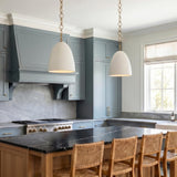A transitional kitchen features the Charlie Pendant 14" in Matte White and Brushed Brass over a black marble island with blue-gray cabinets and woven stools.