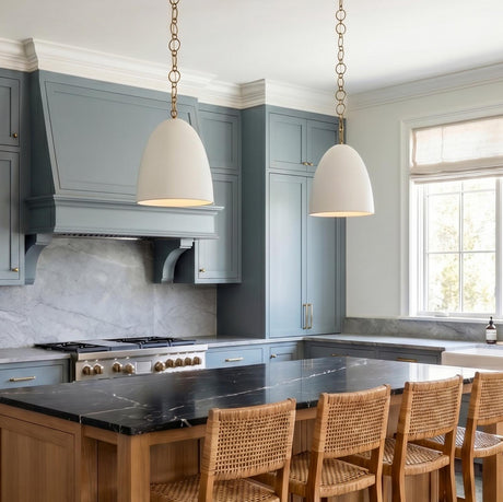 A transitional kitchen features the Charlie Pendant 14" in Matte White and Brushed Brass over a black marble island with blue-gray cabinets and woven stools.