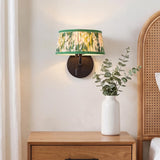 A cottage bedroom with the Daina Wall Sconce 7", Matte Black and Green Floral, installed above a natural wood nightstand next to a rattan headboard.