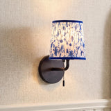 A traditional foyer with the Daina Wall Sconce 10", Matte Black and Blue Floral mounted on a textured beige wallpapered wall above white wainscoting.