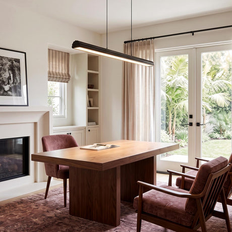 A modern office features a Jacob Linear LED Pendant 48", Matte Black suspended over a walnut desk beside plush armchairs and a fireplace.