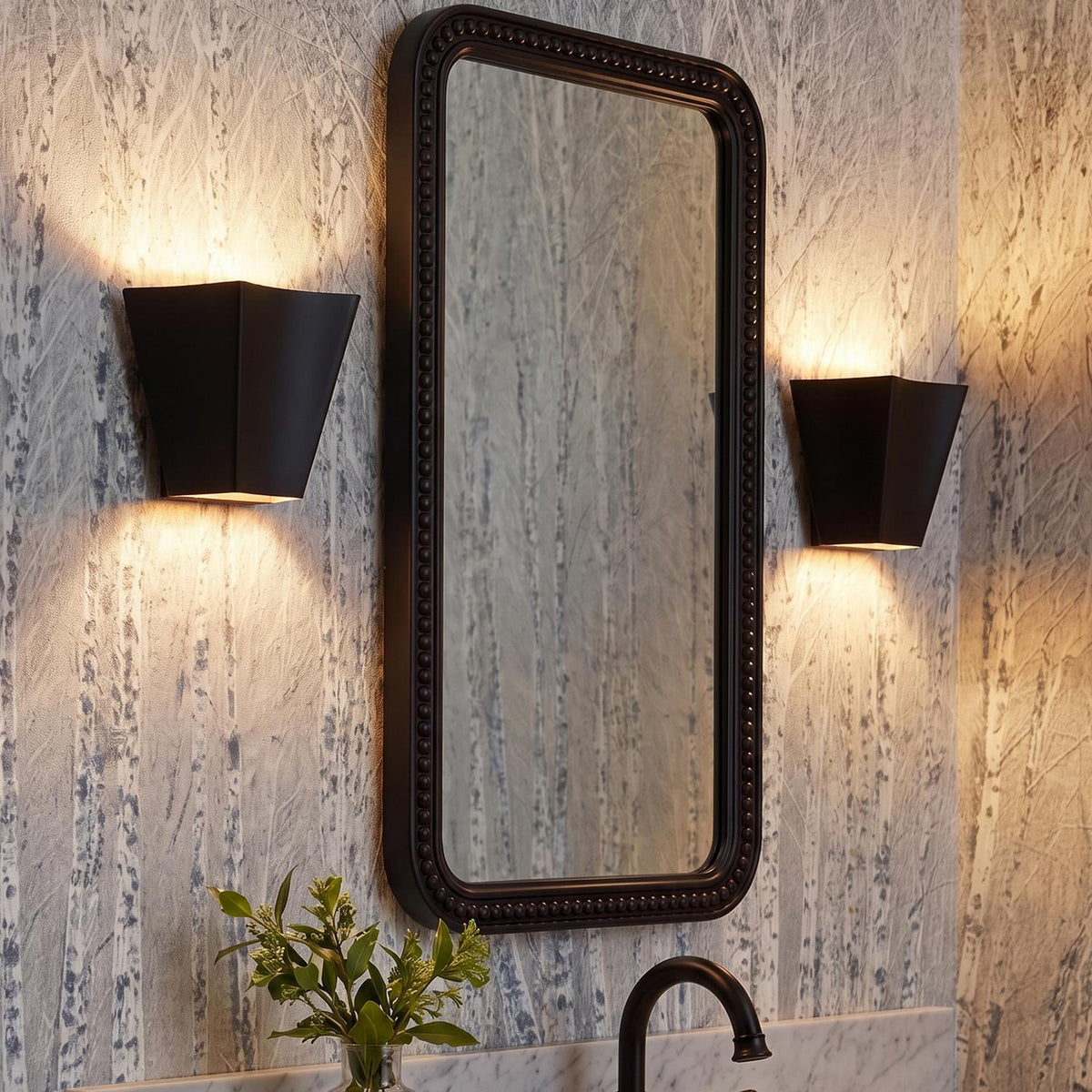 A transitional bathroom with two matte black Brex Wall Sconce 7" fixtures flanking a beaded mirror over a marble countertop with birch tree patterned wallpaper.