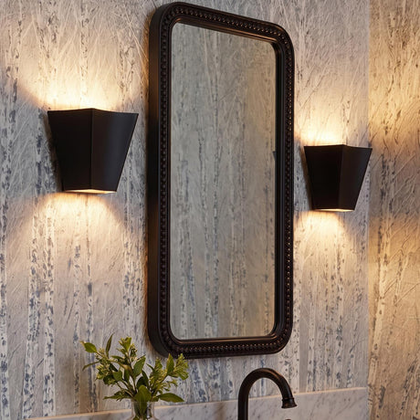 A transitional bathroom with two matte black Brex Wall Sconce 7" fixtures flanking a beaded mirror over a marble countertop with birch tree patterned wallpaper.